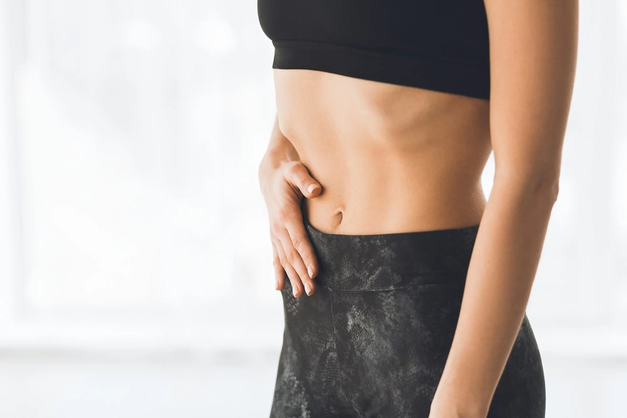 Eine Frau im Sport-BH und Leggings berührt ihren Bauch.