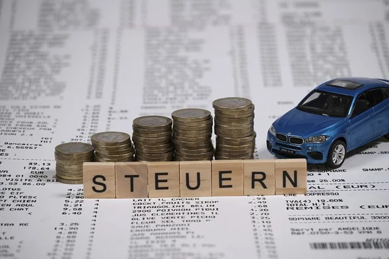 Ein blaues Modellauto, Münzstapel und Holzbuchstaben, die "STEUERN" bilden, auf Rechnungsbelegen liegend.